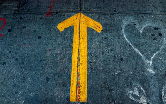 Yellow arrow and white spray-painted hearts on pavement (Unsplash/Jon Tyson)