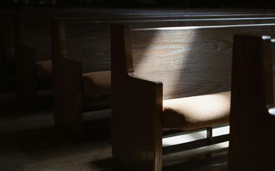 Light shines upon a church pew in a dimly lit church interior. (Unsplash/Josh Applegate)