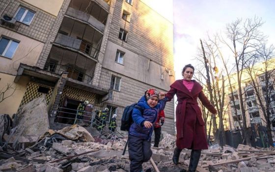 A woman with a child evacuates from a residential building damaged by Russian shelling in Kyiv, Ukraine, March 16. (CNS/Reuters/State Emergency Service of Ukraine)