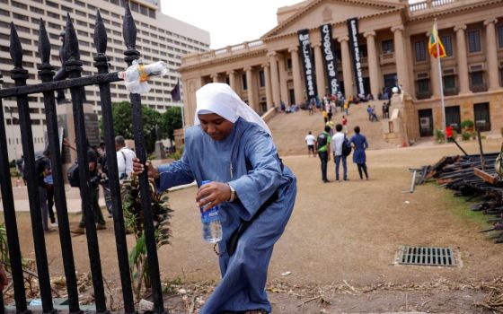 A nun climbs over the boundary wall at the Presidential Secretariat in Colombo, Sri Lanka, July 15, after an official announced the resignation of President Gotabaya Rajapaksa, amid the country's economic crisis. (CNS/Reuters/Dinuka Liyanawatte)