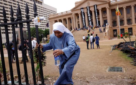 A nun climbs over the boundary wall at the Presidential Secretariat in Colombo, Sri Lanka, July 15, after an official announced the resignation of President Gotabaya Rajapaksa, amid the country's economic crisis. (CNS/Reuters/Dinuka Liyanawatte)