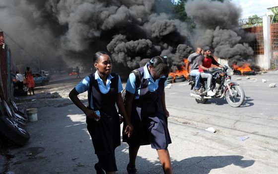 Schoolgirls walk past a burning street barricade during demonstrations Nov. 25, 2021, against widespread kidnappings in Port-au-Prince, Haiti. (CNS/Reuters/Ralph Tedy Erol)