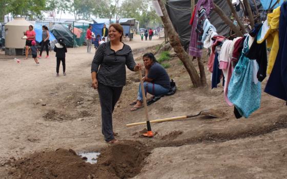 In the Matamoros camp on the Mexican side of the U.S. border, Esmeralda, a community leader from Honduras, pauses in wielding a pickaxe, digging a ditch to keep water runoff from her improvised kitchen from muddying the path below. (GSR/Tracy L. Barnett)