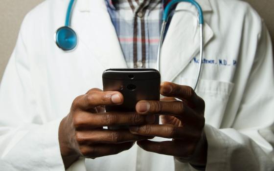 Image of a Black doctor with a smartphone (Unsplash/National Cancer Institutue)