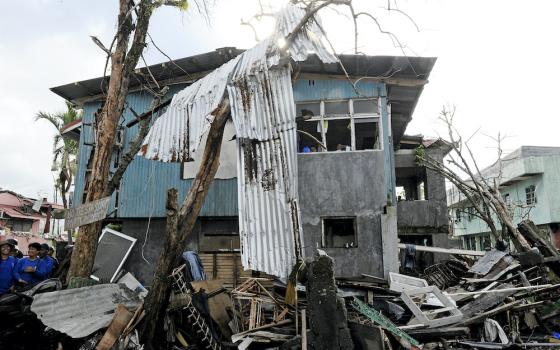 In this 2013 photo, residents of Tacloban peer out of a window of a damaged home as workers helping with clean-up efforts walk through the debris below following Super Typhoon Yolanda/Haiyan. On matters of housing and shelter, the Philippines is vulnerabl
