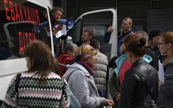 Refugees from war-hit eastern Ukraine stand in line waiting for departure in a refugee center Sept. 15 in Zaporizhzhia, Ukraine. Writing on a bus reads; "Children Evacuation." (AP photo/Andriy Andriyenko)