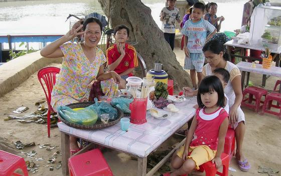 Huynh Thi Phung, a former tuberculosis patient, gives customers a cheery wave while she sells food on the sidewalk in Hoa Vang District of Quang Nam Province, Vietnam. (Joachim Pham)