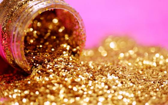 Image: A bottle of gold glitter lies on its side, glitter in a pile on a pink background.