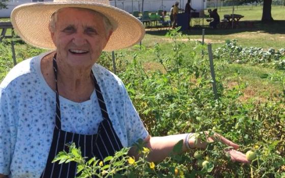 Jeanne Clark in a garden, wearing a straw hat and holding produce